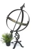 A black metal sundial with Roman numerals and a small potted green plant next to it, set against a white background. Anteprima dell’immagine prodotto