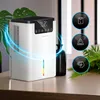 A white dehumidifier is shown on a wooden table, with plants in the background. There are informational icons on the right side of the image. Náhled obrázku produktu