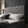 A close-up view of a bed with a gray upholstered headboard and pillows. Produktbild-Vorschau