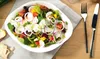 A close-up overhead shot of a salad in a white bowl, set on a wooden table with a grey napkin and cutlery. Voir les images du produit