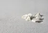 Several small white stones are scattered on a light gray, textured surface. Produktbild-Vorschau