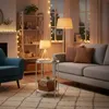 A cozy living room scene at night, with warm lighting from lamps and string lights. Produktbild-Vorschau