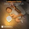 A baby sleeping next to a night light on a bed. Voir les images du produit