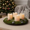 A festive Christmas scene with an advent wreath centerpiece on a table, a decorated Christmas tree in the background, and a cozy blanket draped over a chair. Produktbild-Vorschau