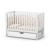A white baby crib with a beige mattress and a drawer underneath, shown on a white background. Anteprima dell’immagine prodotto