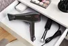 A black Rowenta hairdryer with pink accents is placed in an open drawer, alongside a round brush and its power cord. A makeup palette and a diffuser attachment are visible in the background. Anteprima dell’immagine prodotto