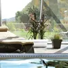 A lounge chair and potted plants are placed near a large window overlooking a garden. Produktbild-Vorschau