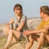 A man and a woman sitting on a sandy dune, holding metal water bottles. Náhled obrázku produktu