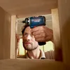A man is using a Bosch cordless drill to screw a piece of wood into a cabinet. Náhled obrázku produktu