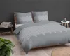 A bed with grey bedding featuring a white peacock feather pattern, set against a dark grey wall. Produktbild-Vorschau