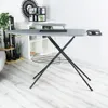 An ironing board is set up in a room with shelves and plants in the background. Voir les images du produit