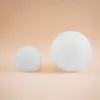 Two white spheres of different sizes are placed on a light peach background. Produktbild-Vorschau