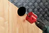 A drill with a hole saw attachment is drilling a hole in a wooden surface, with a metal surface visible in the background. Anteprima dell’immagine prodotto