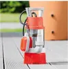 A submersible pump sits on a wooden deck next to a large orange container.