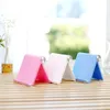 Three colorful phone stands are displayed on a wooden surface in front of a window with a blurred background. Náhľad obrázku produktu