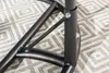 Close-up of the black metal frame of a hanging chair, showing the connection points with bolts and nuts, resting on a patterned rug. Produktbild-Vorschau