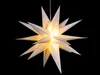 A white star-shaped lantern with small star cutouts, illuminated from within, against a black background. Produktbild-Vorschau