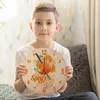 A young boy is holding a round wall clock with a cocktail design in front of him. Produktbild-Vorschau