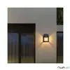 A black solar wall light is mounted on a light gray wall, illuminating the area with warm light. Produktbild-Vorschau
