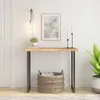 A console table with a wooden top and metal legs, decorated with a plant, picture frame, and candles, placed in a room with a door and a plant. Produktbild-Vorschau