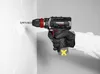 A person wearing gloves is using a cordless drill to make a hole in a white tiled wall. Produktbild-Vorschau