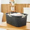 A dark gray laundry basket filled with folded towels sits on a wooden surface in a bathroom setting. Produktbild-Vorschau