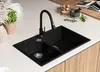 A black double basin kitchen sink with a black faucet is shown on a white countertop, with wooden cabinets visible below. Produktbild-Vorschau