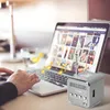 A person's hands are on a laptop keyboard, with a small silver speaker cube next to it. Musical notes are floating around the speaker and laptop. Produktbild-Vorschau