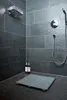 A modern shower stall with dark gray tiled walls and floor, featuring a shower mat, two bottles of shampoo, and a shower head. Produktbild-Vorschau