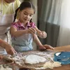 A young girl and an adult are making dumplings on a wooden table covered in flour. Podgląd zdjęcia produktu