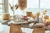 A dining table set for a meal with plates, bowls, cutlery, and decorative dried flowers. Produktbild-Vorschau
