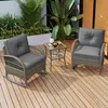 A rattan balcony set with gray cushions and a small glass-topped table is placed on a wooden deck, surrounded by lush green plants. Podgląd zdjęcia produktu