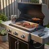 A grill with food cooking on it, set up on a wooden deck. Produktbild-Vorschau