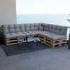 A sectional sofa made of pallets with gray cushions sits on a balcony overlooking the ocean. Anteprima dell’immagine prodotto