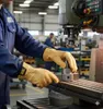 A person wearing work gloves and a blue uniform operates a milling machine in a factory setting. Produktbild-Vorschau