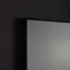 A close-up view of the corner of a mirror with a black frame, set against a dark, textured wall. Produktbild-Vorschau