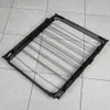 A black metal drying rack is shown folded on a tiled floor. Náhľad obrázku produktu