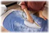 A person is ironing blue fabric on an ironing board with a steam iron. Voir les images du produit