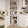 A tall, white, multi-tiered shelf unit filled with various jars and containers is placed in a kitchen setting next to a counter with a sink. A portion of a living room with a sofa is visible on the left. Podgląd zdjęcia produktu