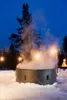 An inflatable hot tub is set up outdoors in the snow at dusk, with steam rising from the water and string lights illuminating the scene. Náhled obrázku produktu