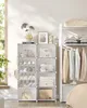 A white modular shelving unit filled with folded clothes, shoes, and a handbag, next to a clothing rack with hanging garments. Náhled obrázku produktu