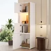 A tall white cabinet with natural wood accents, open doors revealing shelves with books and decor, placed near a window with greenery outside and a decorative lamp and side table nearby. Anteprima dell’immagine prodotto
