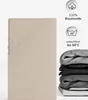 A folded beige fitted sheet is shown on the left, with icons and text indicating product features on the right. A stack of folded sheets in various gray tones is also visible on the right. Produktbild-Vorschau