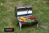 A portable charcoal grill filled with food, placed on a grassy lawn. Náhled obrázku produktu