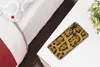 A phone with a leopard print case rests on a white table next to a plant and a bed. Produktbild-Vorschau