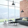 A living room with a large window offering a view of rolling hills, a grey sofa, a floor lamp, a coffee table, and a white fan. Produktbild-Vorschau
