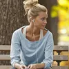 A young woman with blonde hair in a messy bun sits on a park bench, wearing earphones and looking to the side. Náhľad obrázku produktu