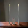 Two white LED taper candles with a remote control placed between them on a wooden surface. Produktbild-Vorschau