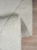 A close-up view of a shaggy rug with a diamond pattern, partially folded to reveal the backing. Produktbild-Vorschau