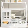 A white wooden children's bed with a house-like frame, featuring a window detail and storage drawers underneath. The bed is made up with pillows and a blanket. Voir les images du produit